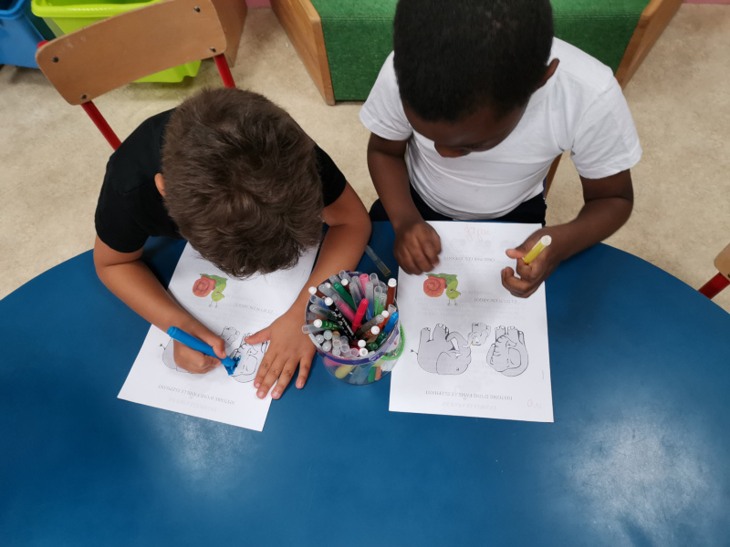 Deux enfants assis à une table dessinent sur des feuilles avec des feutres.
